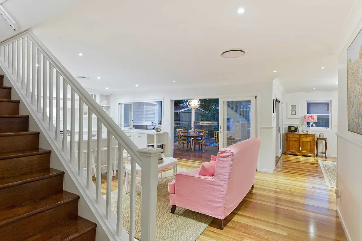Bright living and dining room with a white staircase, sofa, wooden floor and a view onto a terrace